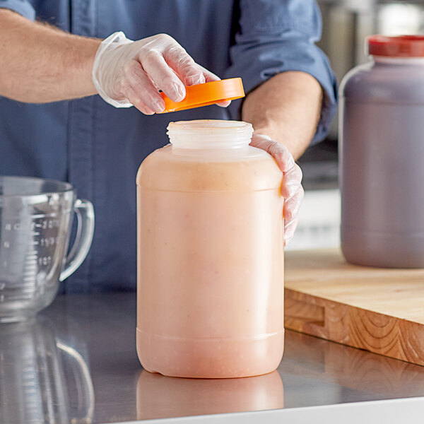 A large one-gallon plastic backup container with an orange cap being opened by a person wearing gloves.