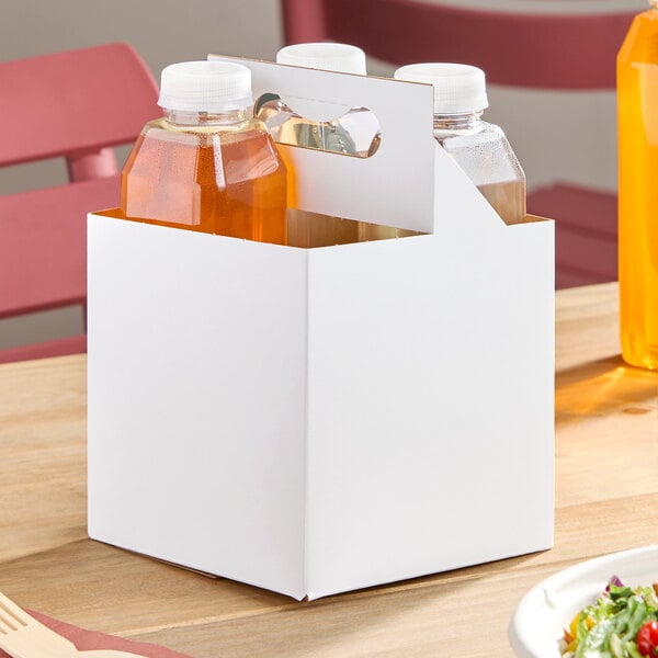 A white cardboard beverage carrier with a handle, holding four 16 oz. bottles.