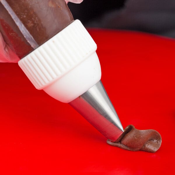 A metal curved petal piping tip attached to a piping bag dispensing chocolate frosting onto a red surface.