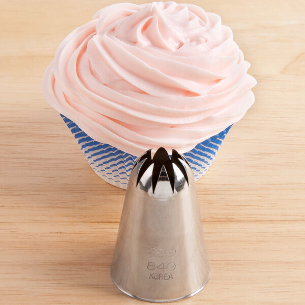 A stainless steel closed star piping tip is shown in front of a cupcake with pink frosting.