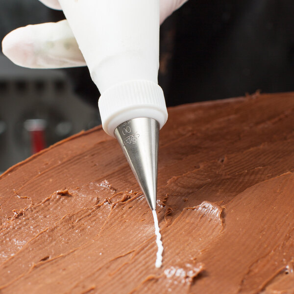 A metal piping tip attached to a piping bag is being used to decorate a chocolate-frosted cake.