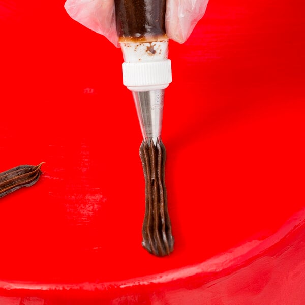 An open star piping tip being used to pipe chocolate frosting onto a red surface.