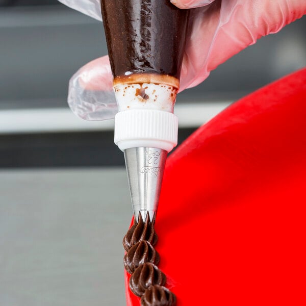 An open star piping tip being used to pipe chocolate frosting onto a cake.