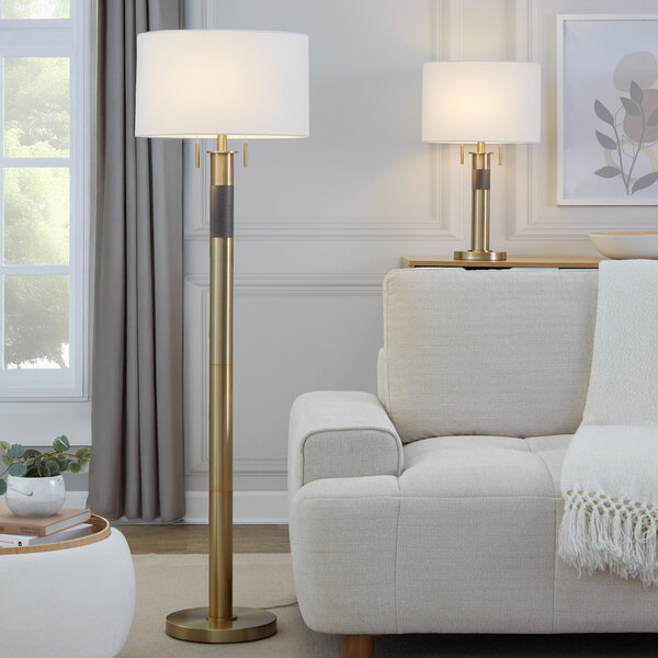 A gold table lamp with a white linen drum shade.