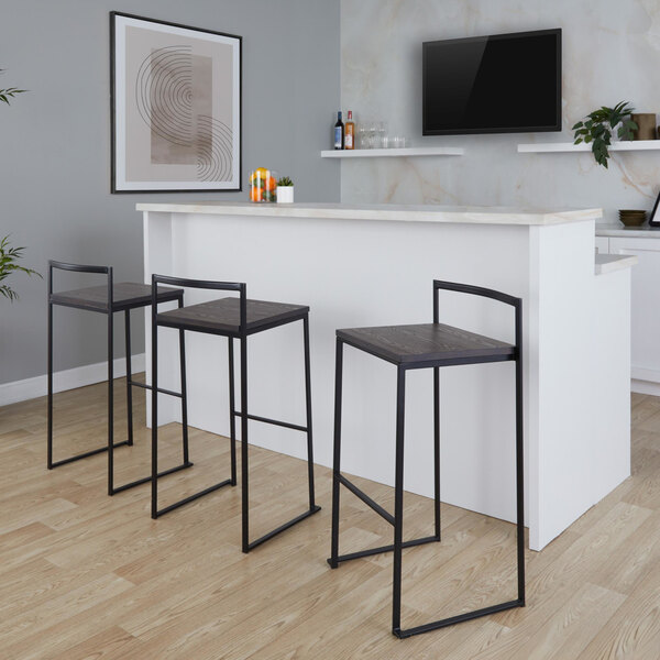 A set of black metal stackable low-back barstools with espresso bamboo seats placed at a white bar counter.