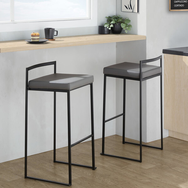 A pair of black metal barstools with low backs and gray faux leather seats.