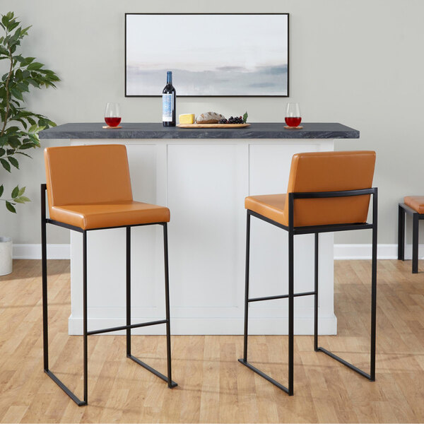 A pair of high-back barstools with black metal frames and camel-colored faux leather seats and backs.