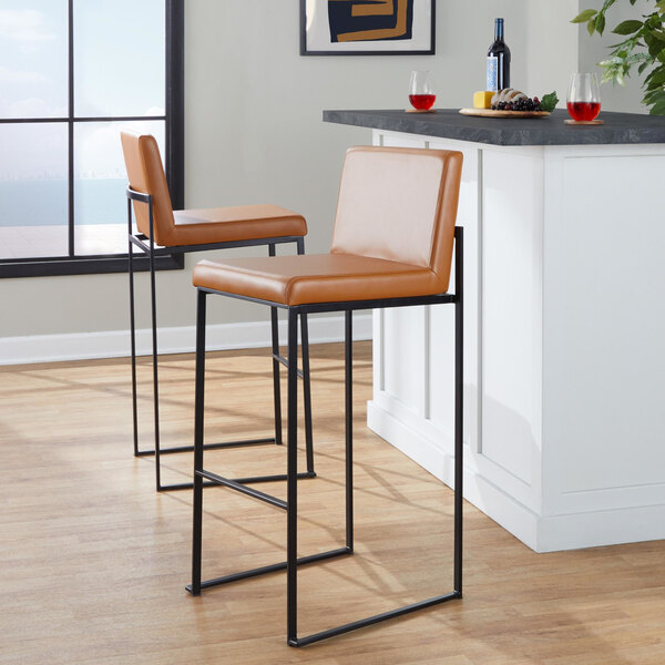 A pair of high-back barstools with black metal frames and camel-colored faux leather seats and backs.