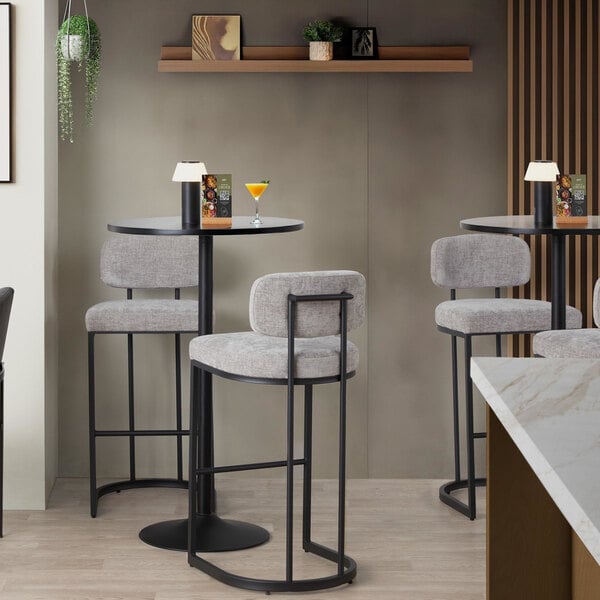 A pair of modern barstools with black metal frames and light gray fabric seats and backs, placed at a high-top table in a contemporary setting.