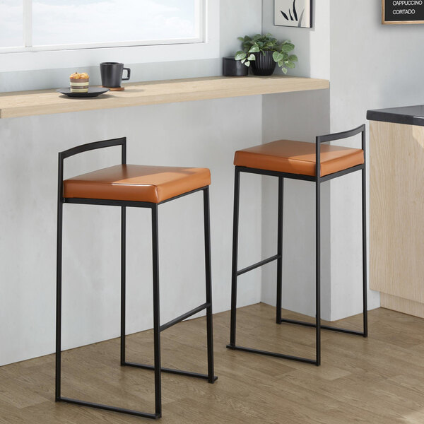 A pair of modern barstools with black metal frames and camel-colored faux leather seats.