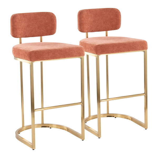 A pair of barstools with gold metal frames and salmon-colored fabric seats and backs.
