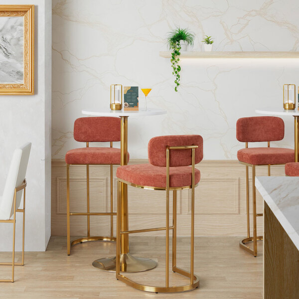 A gold metal barstool with a salmon fabric back and seat.