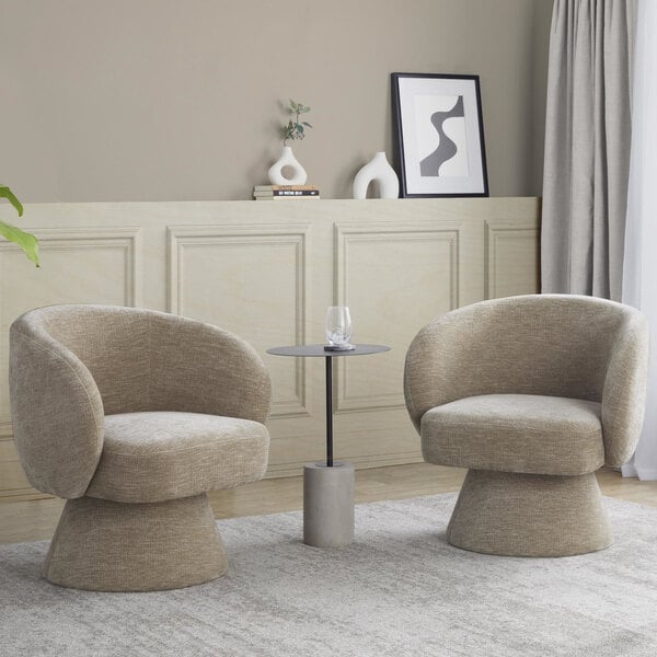 A pair of light brown fabric swivel accent arm chairs with pedestal bases are positioned around a small round side table in a modern living room setting.