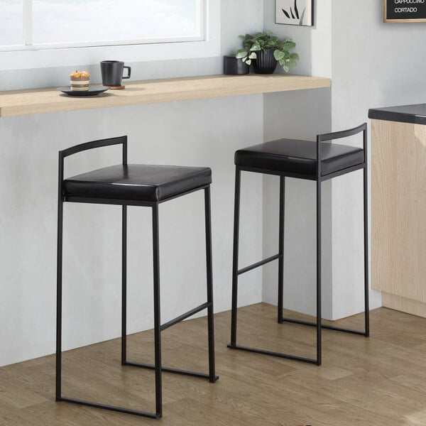 A pair of black metal stackable low-back barstools with black faux leather seats.