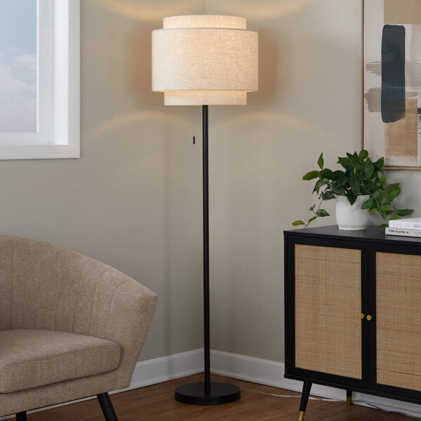 A black floor lamp with a beige linen tiered shade.