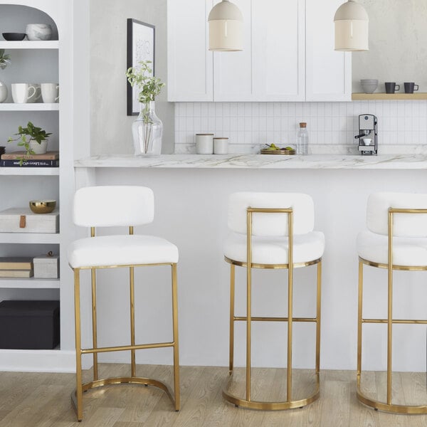 A set of barstools with gold metal frames and white faux leather seats and backs.