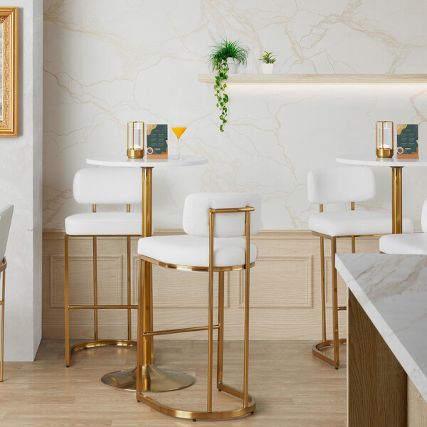 A modern barstool with a gold metal frame and white faux leather back and seat.