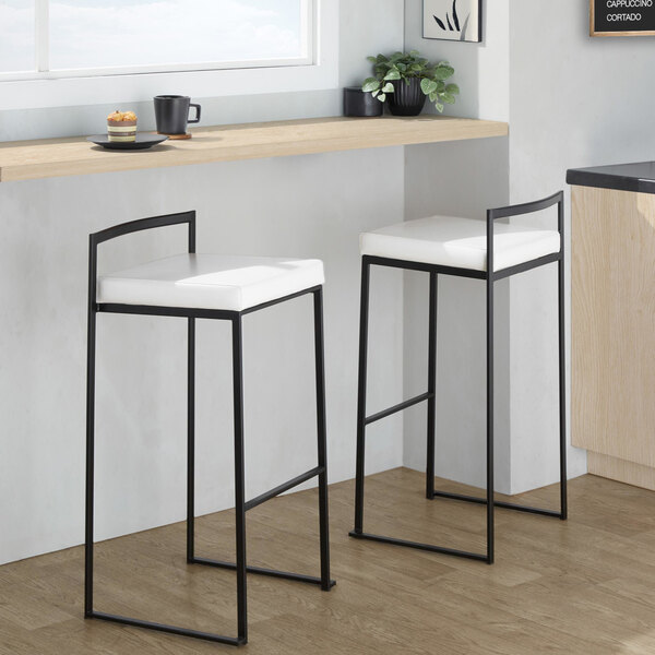 A pair of black metal barstools with low backs and white faux leather seats.