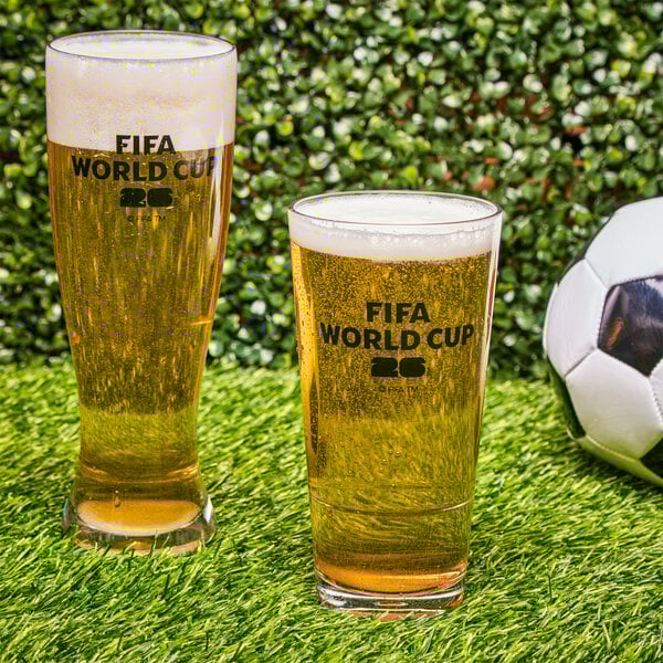A clear plastic pilsner glass with a black FIFA World Cup 2026 logo, filled with beer and foam.