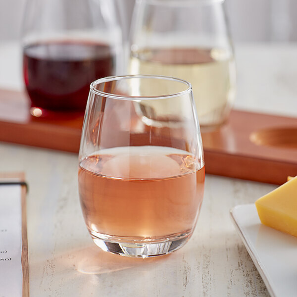 A clear stemless wine tasting glass filled with rosé wine.