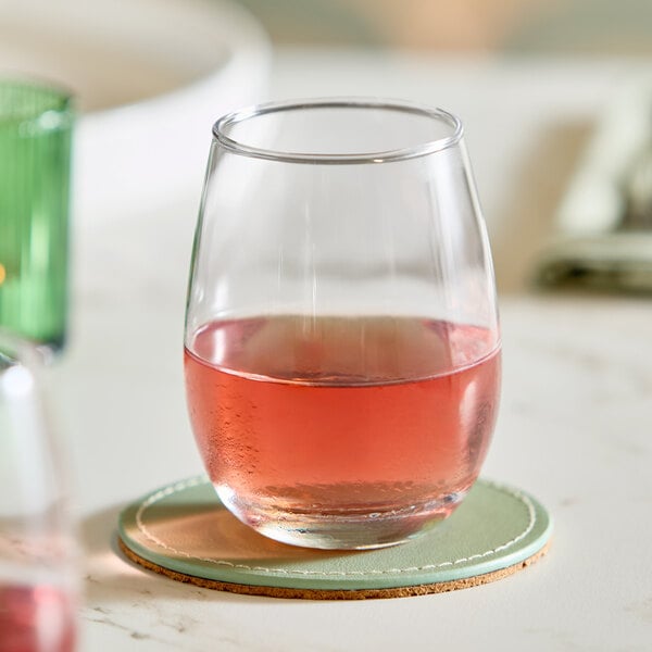A clear 9 oz. stemless wine glass partially filled with a pink beverage, placed on a round coaster.