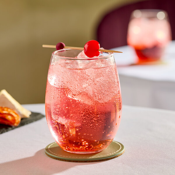 A clear, stemless wine glass filled with a pink sparkling beverage, ice, and garnished with cherries on a cocktail pick.