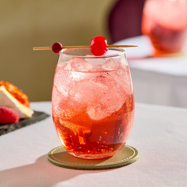 A clear stemless wine glass filled with a red iced beverage and garnished with two cherries on a skewer.