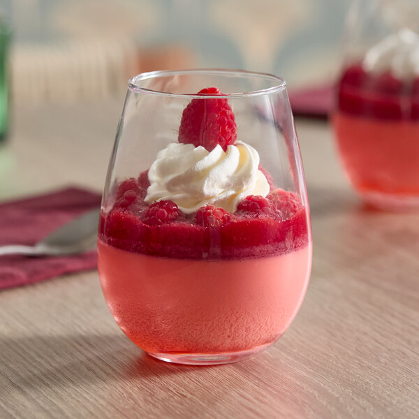 A clear stemless wine glass filled with a pink dessert, topped with whipped cream and raspberries.
