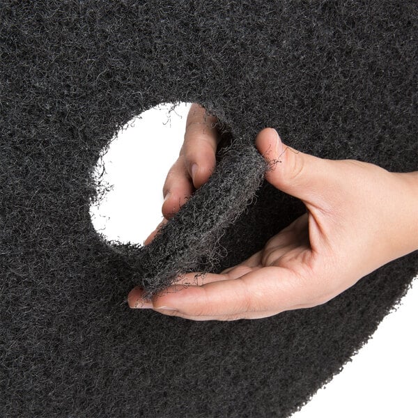 A round black stripping floor pad with a removable center section, shown being held by a hand.