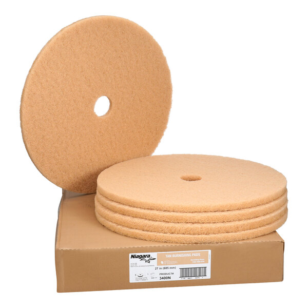 A set of five large tan circular floor burnishing pads with center holes, displayed on a cardboard box.