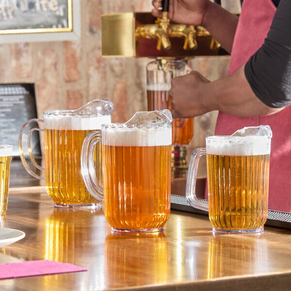 A clear 60 oz. plastic beverage pitcher filled with beer, shown on a bar counter.