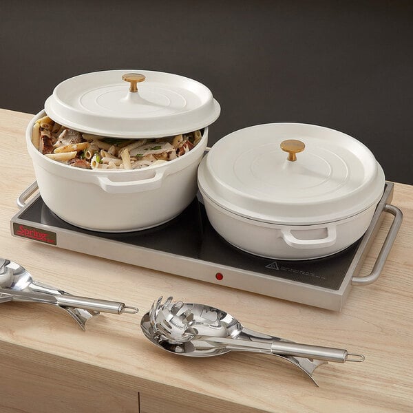A white non-stick round casserole dish with a cover and gold knob, shown on a countertop with food inside.