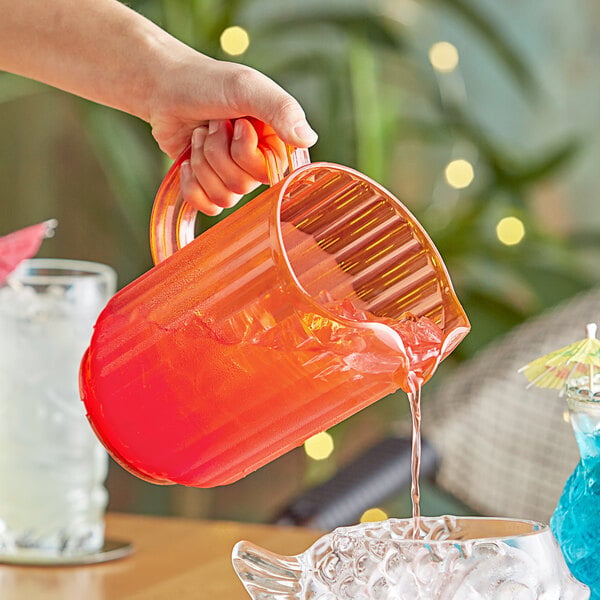 A coral-colored plastic beverage pitcher being used to pour a drink.