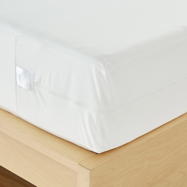 A white waterproof poly knit mattress protector covering a full XL mattress on a wooden bed frame.