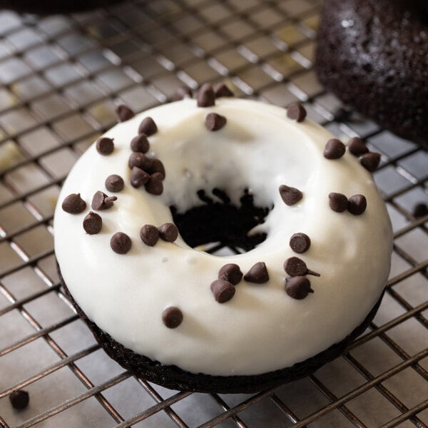 A chocolate donut topped with white icing and chocolate chips on a cooling rack.