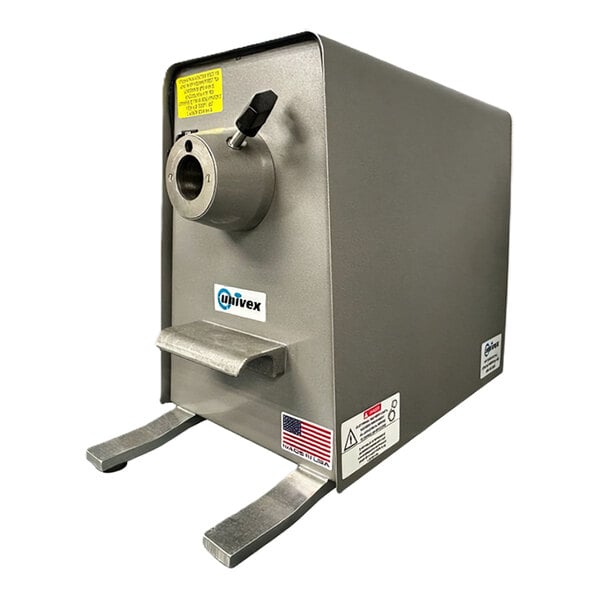 A metallic, box-shaped machine with a circular opening, lever, and two sturdy legs, featuring warning labels and a small American flag sticker on the front.