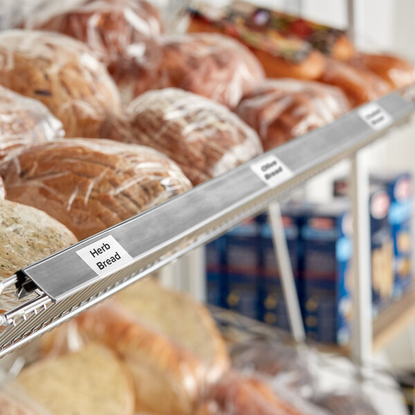 A gray clip-on label holder attached to a wire basket shelf, used for organizing and labeling products such as bread.