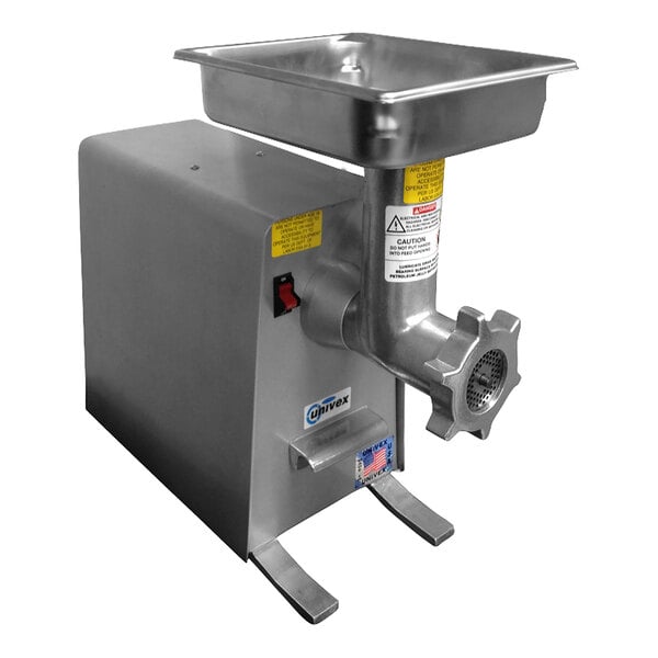 A stainless steel electric meat grinder with a rectangular tray on top and a front grinding plate, featuring warning labels and a power switch.