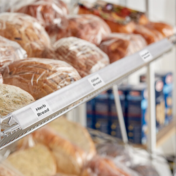 A clear clip-on label holder attached to a wire basket shelf displaying various types of bread.