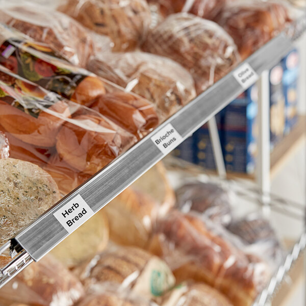 A gray clip-on label holder attached to wire basket shelving, used for organizing and labeling products such as bread.