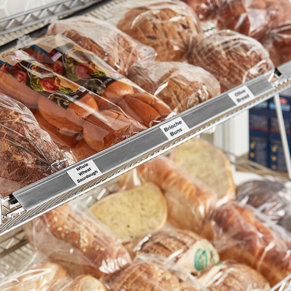 A gray clip-on label holder attached to wire basket shelving, used for organizing and labeling bakery products.