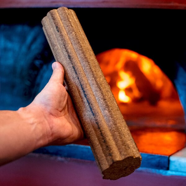 A hand holding a white oak wood fire log in front of a lit fireplace.