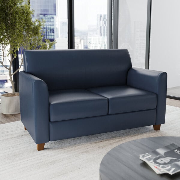 A navy blue leather loveseat with wooden feet.