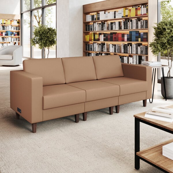 A three-seat cognac-colored leather sofa with wooden feet and built-in charging banks.
