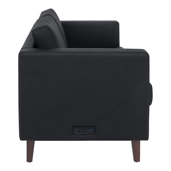 A black loveseat with wooden feet and a built-in charging bank on the side.