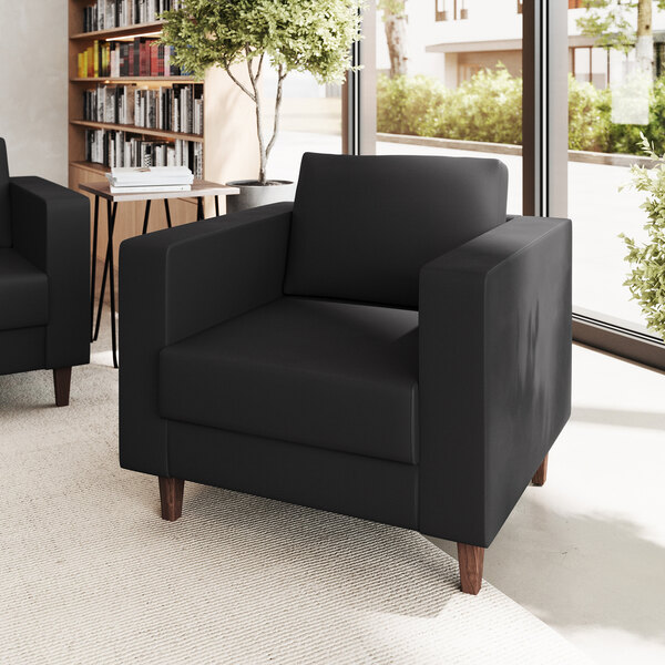 A black armchair with a boxy design, wooden legs, and a built-in charging bank.