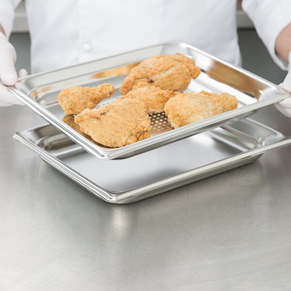 A person holding a tray of fried chicken in a Vollrath stainless steel hotel pan.