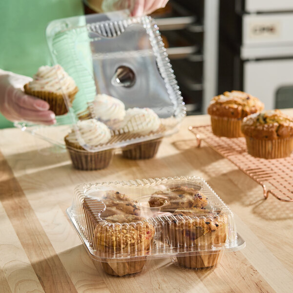 A clear plastic hinged container with four compartments, each holding a jumbo cupcake or muffin, and a medium dome lid.