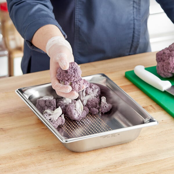 A person in gloves uses a knife to cut purple cauliflower on a cutting board.