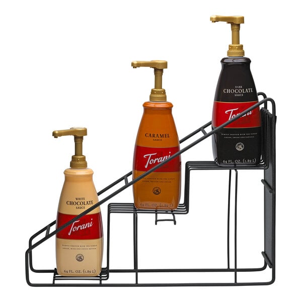 A black stainless steel wire rack holding three 64 oz. Torani flavoring sauce bottles in white chocolate, caramel, and dark chocolate flavors.